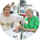 Un grupo de adultos mayores riendo y disfrutando de una comida juntos en Eishel. Enlace a la sección de vida social de nuestros servicios.